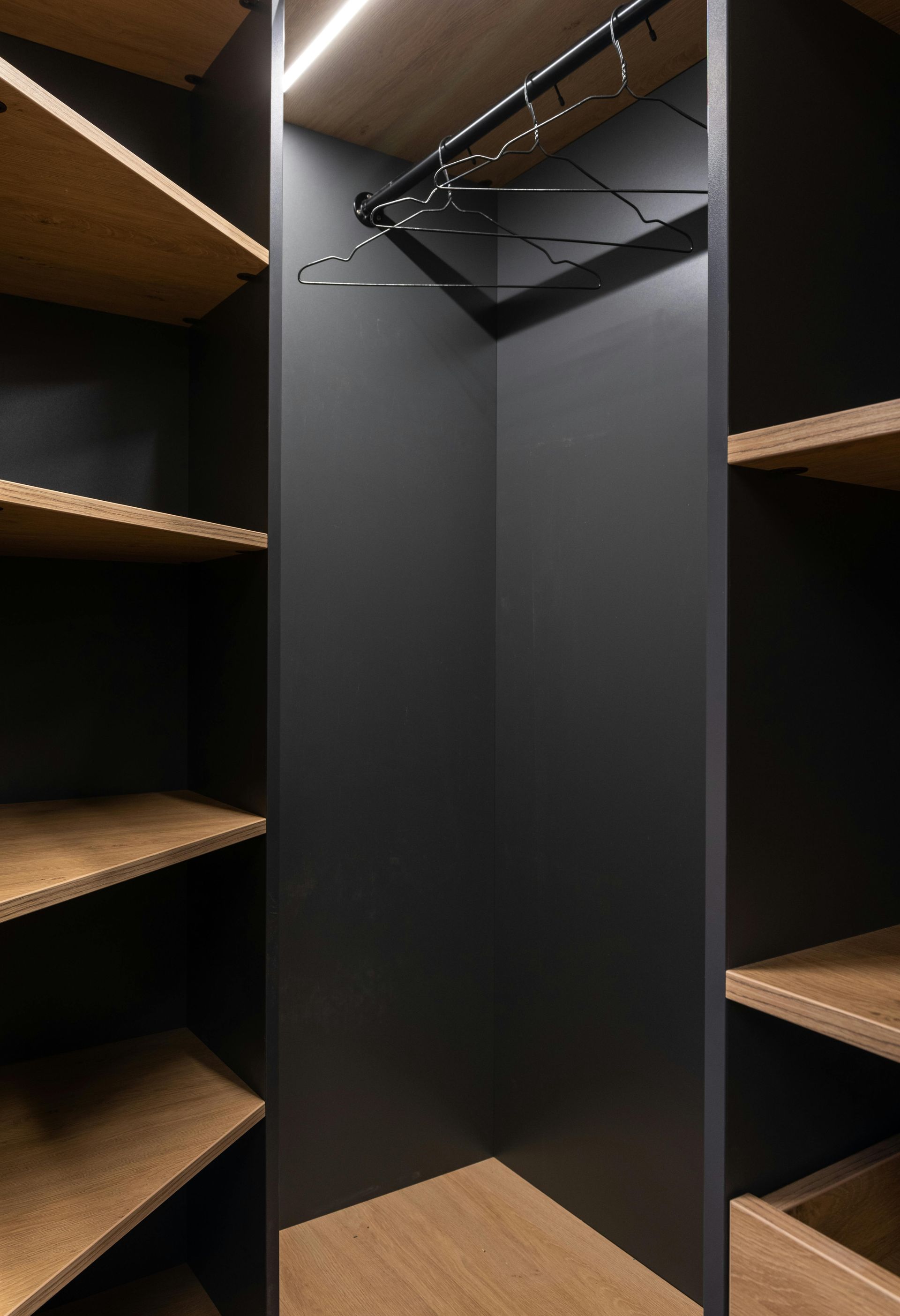 Built-in closet with dark gray walls and wooden shelves. Clothes hangers are mounted at the top.