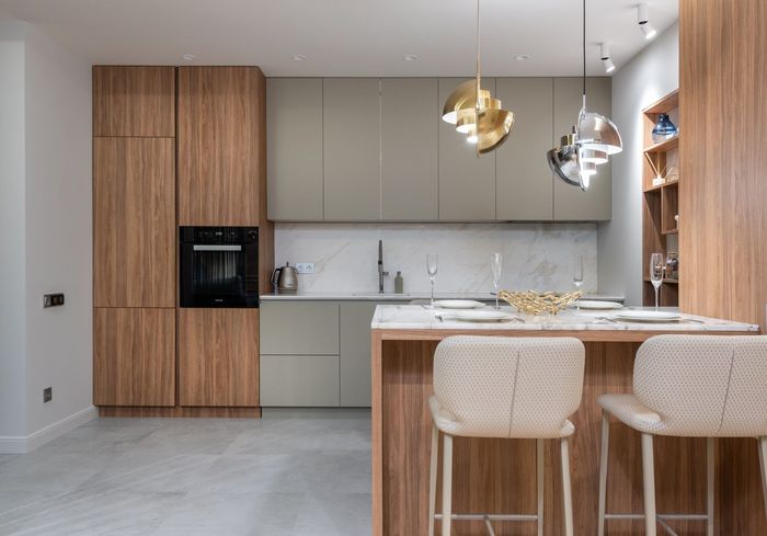 Modern kitchen with wood and gray cabinetry, marble backsplash, island, and hanging lights.