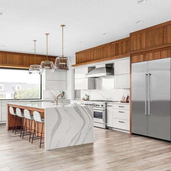 Modern kitchen with white cabinets, wood accents, marble countertops, and stainless steel appliances.
