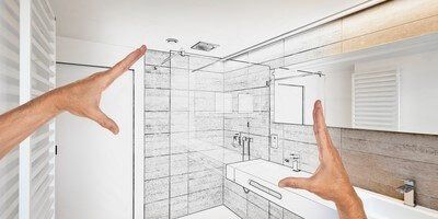 Hands framing a bathroom sketch. Shower, sink, and mirror visible.
