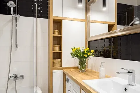 Modern bathroom with a white tile shower, wooden vanity, and decorative shelves.