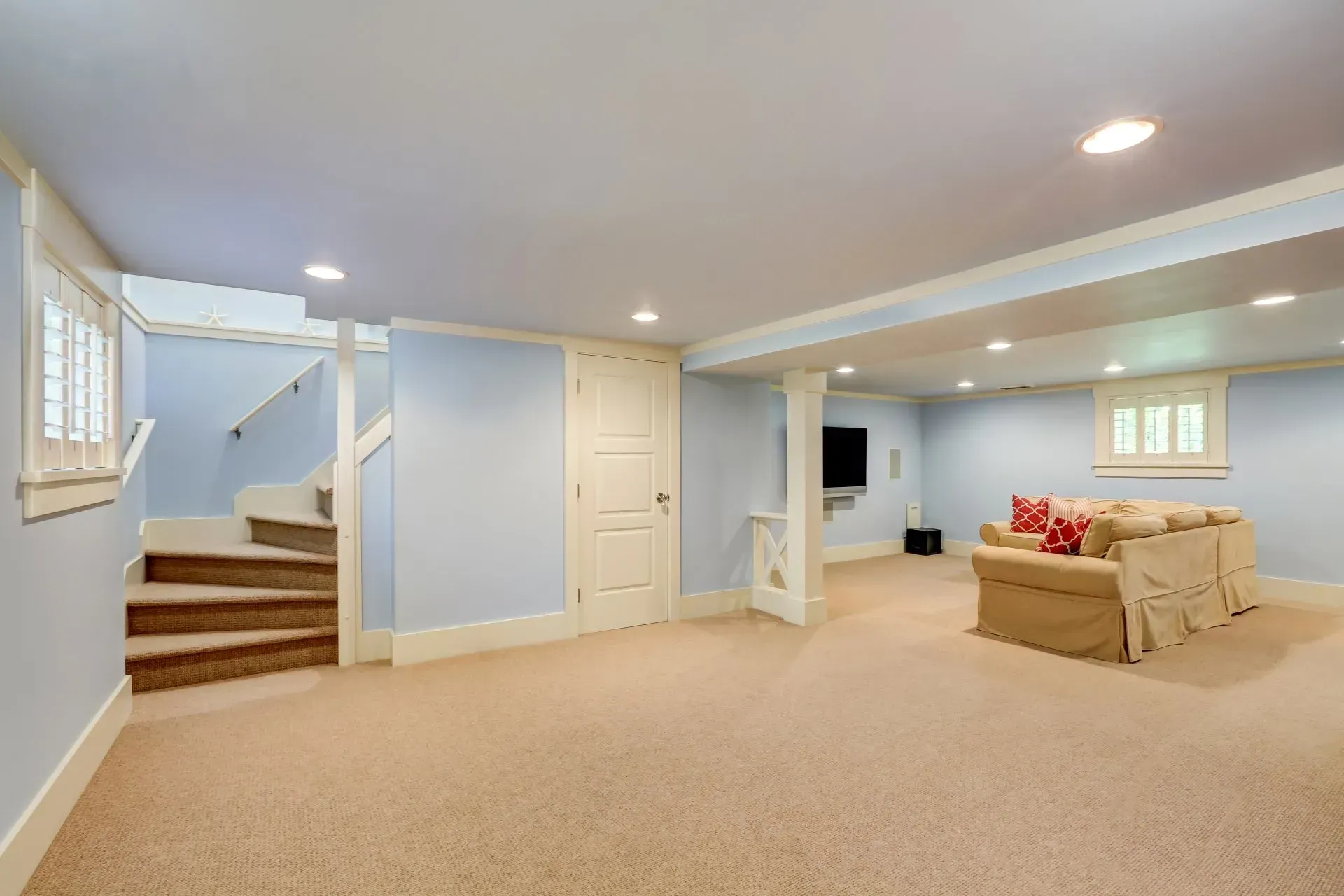Basement room with stairs, light blue walls, tan carpet, and a beige sofa.