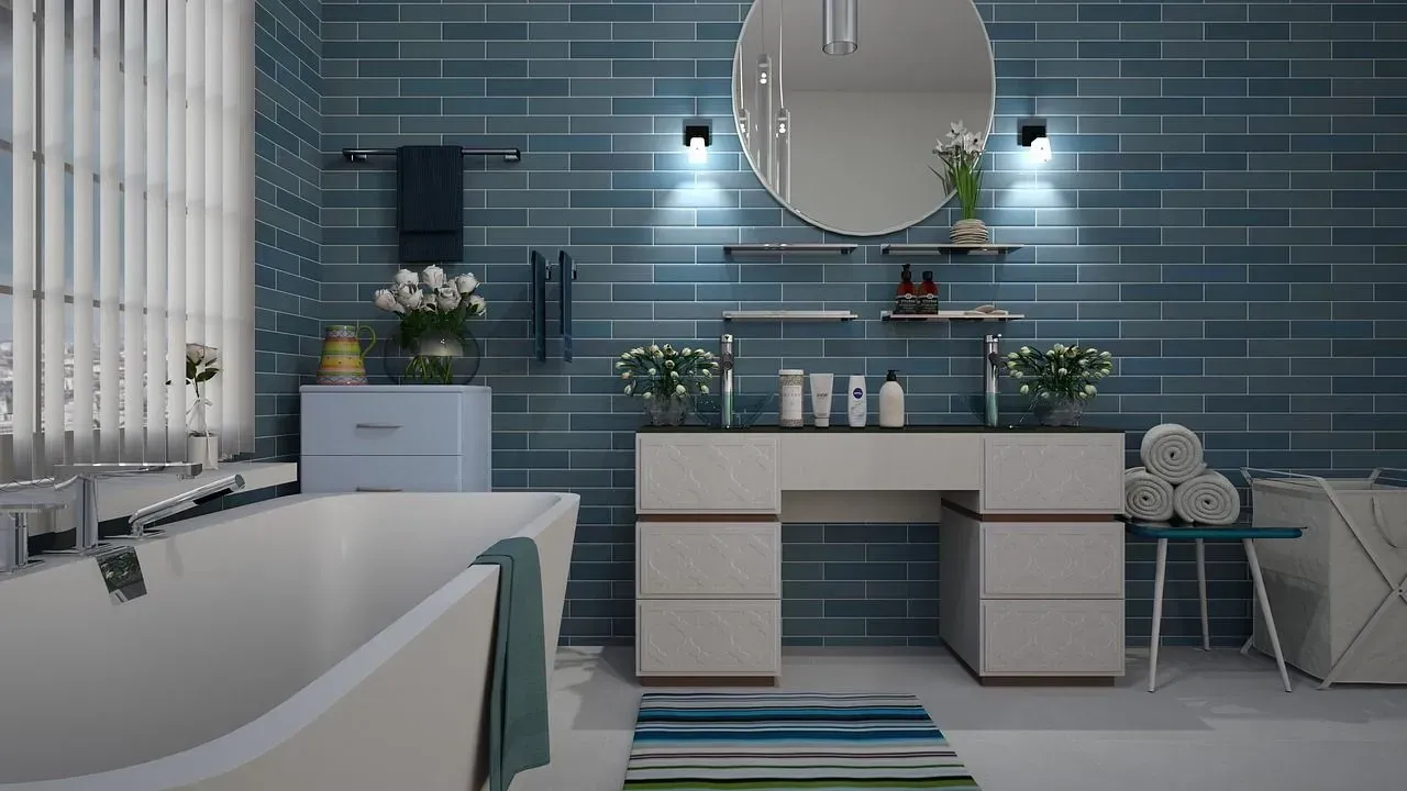 Bathroom with blue tiled walls, white tub, vanity, and round mirror.