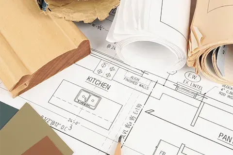 Blueprints, wood trim, and paint swatches on a white surface, representing home renovation planning.