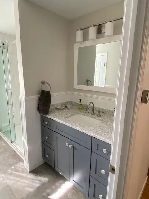 Bathroom with gray vanity, granite countertop, mirror, and white trim. Shower visible to the left.