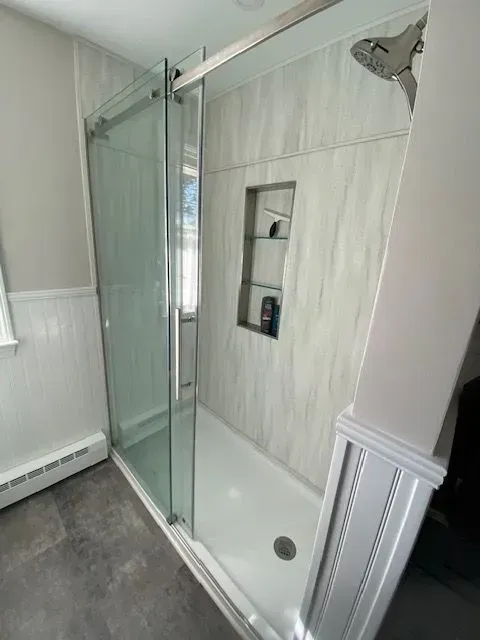 Shower with sliding glass doors, built-in shelving, and gray and white marbled wall panels.