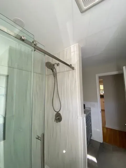 Shower with sliding glass door, white tiled walls, and silver shower head in a bathroom.