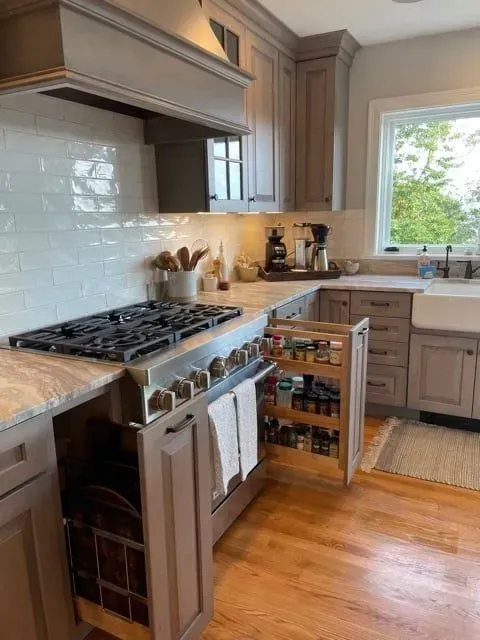 Kitchen with gray cabinets, stovetop, spice rack, white backsplash, and wooden floors.