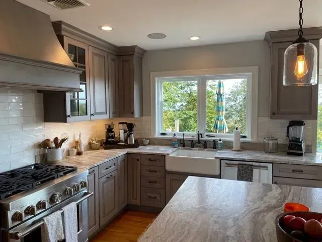 Kitchen with gray cabinets, marble countertops, stainless steel appliances, and a window overlooking trees.