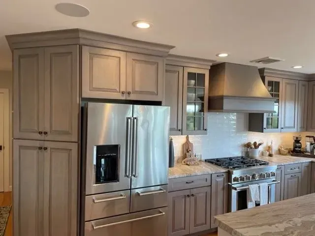 Kitchen with gray cabinets, stainless steel refrigerator, and range. White backsplash, granite countertops.