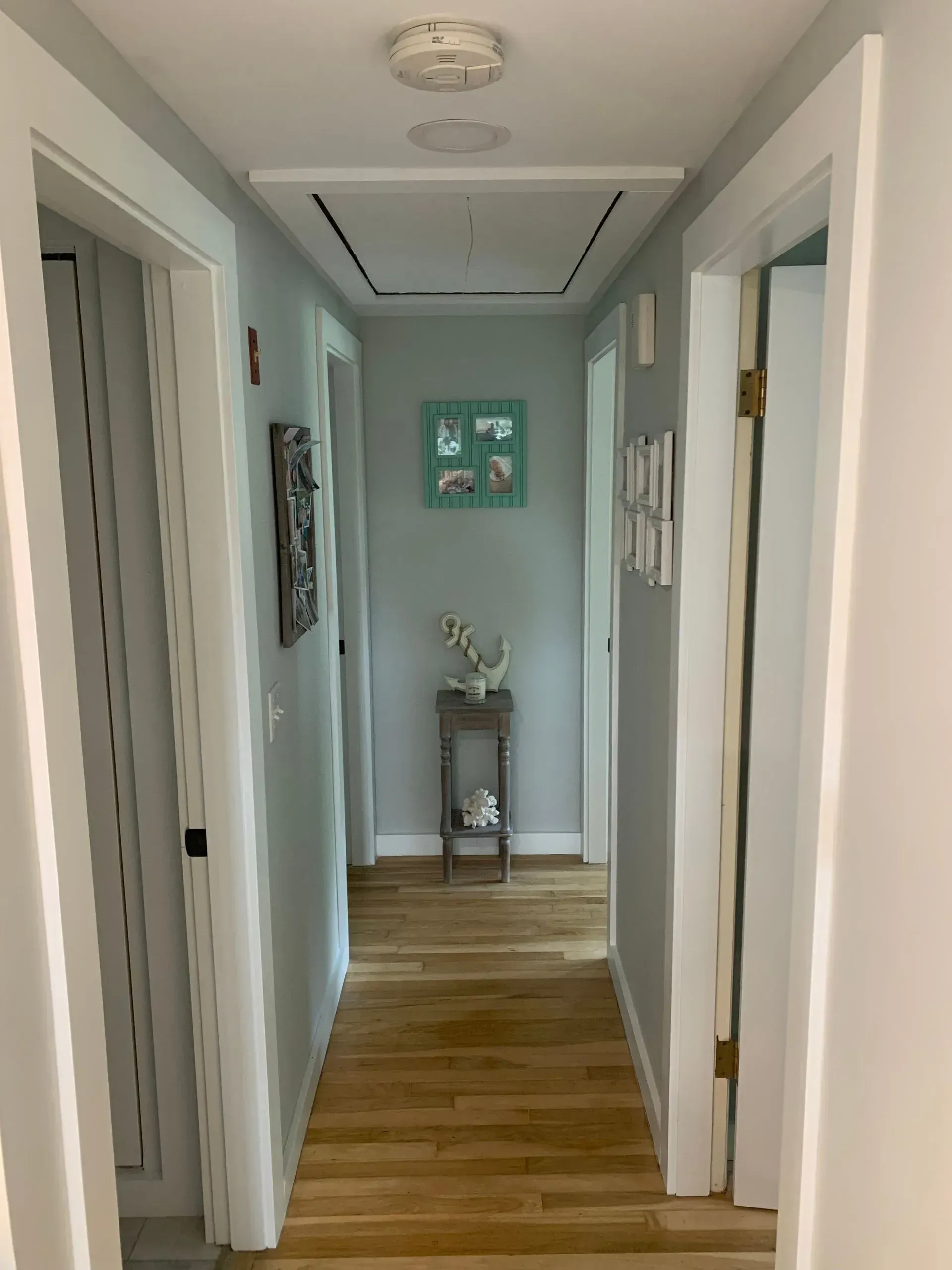 Narrow hallway with light blue walls, wooden floor, and doors on either side.