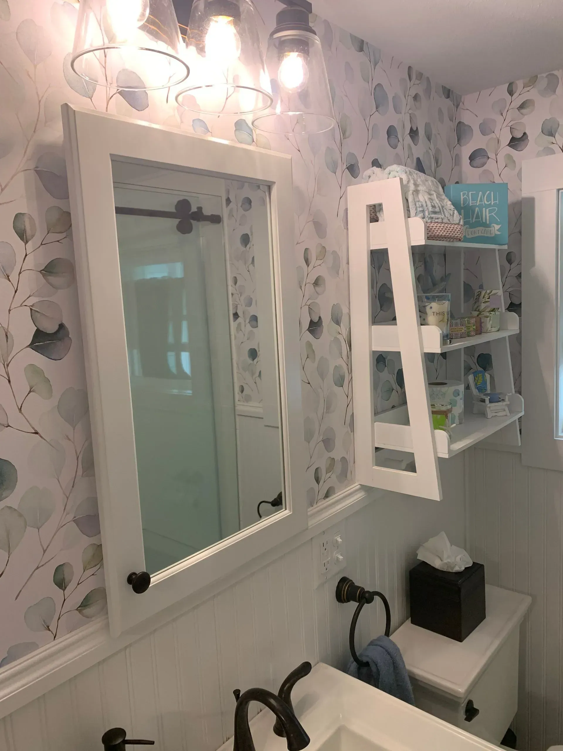 Bathroom with floral wallpaper, white mirror, and a small ladder shelf.