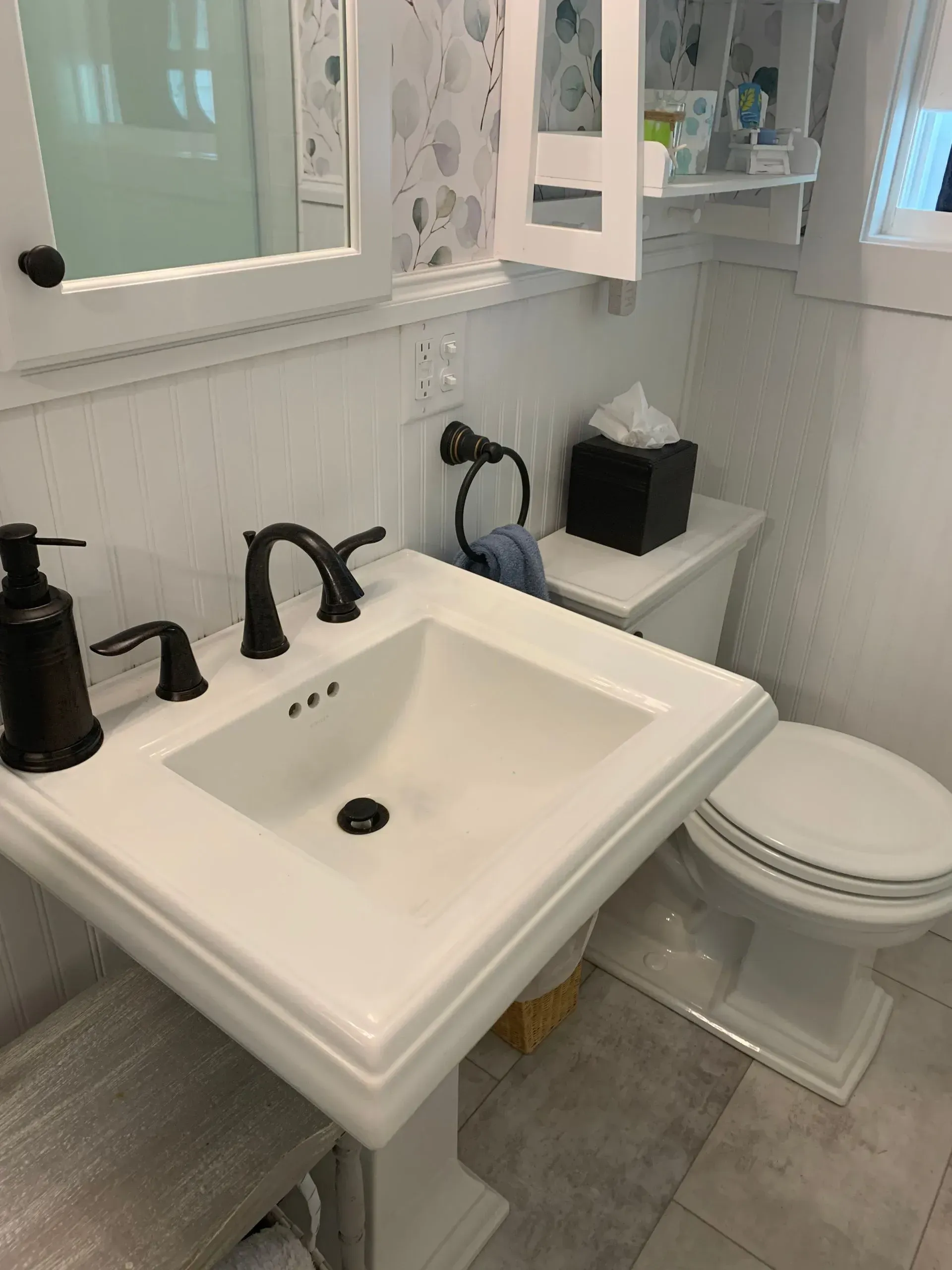 White bathroom sink and toilet with black fixtures, tissue box, and mirror.