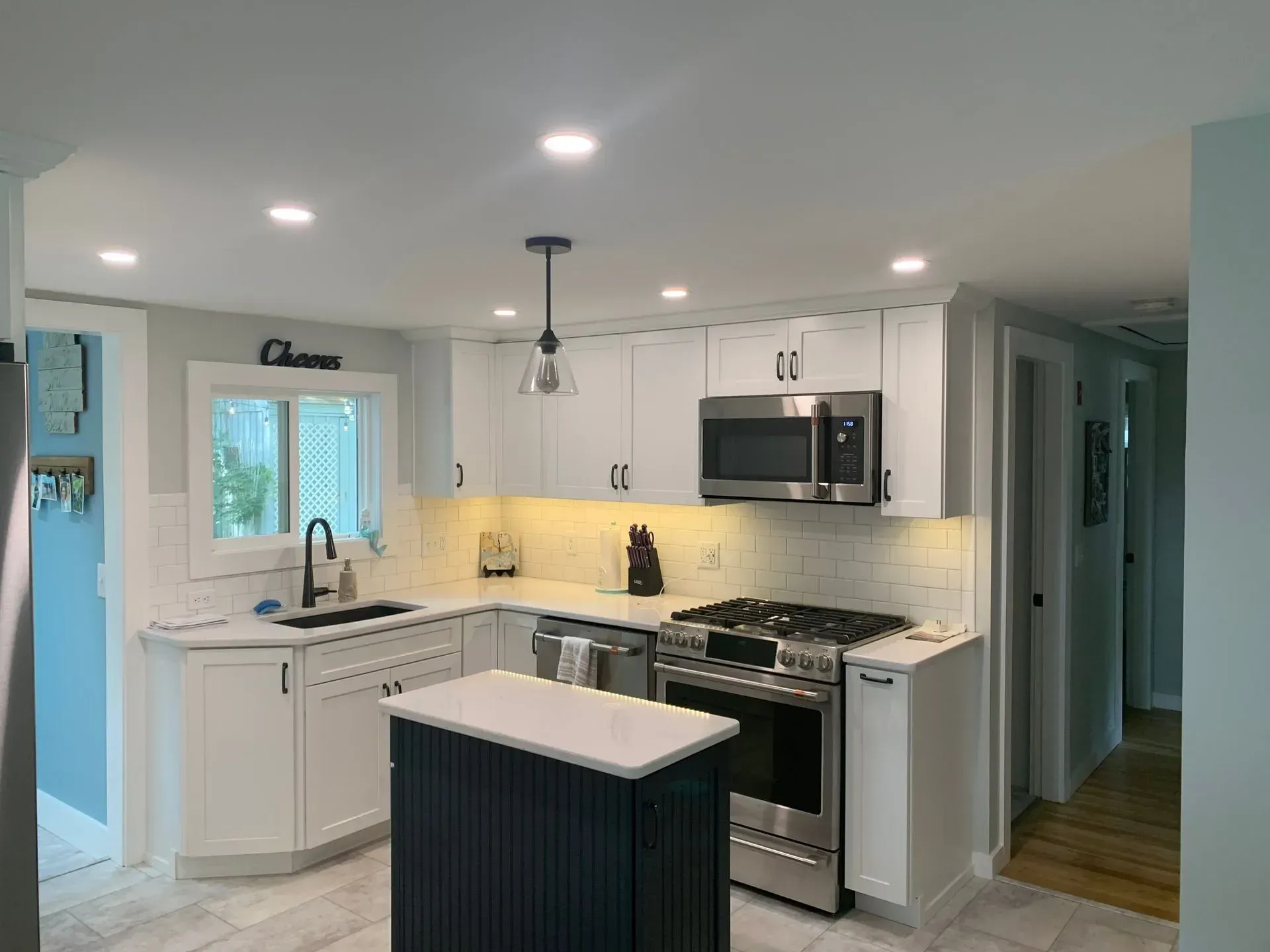 Spacious kitchen with gray cabinets, island, stainless appliances, and granite countertops. Three wooden bar stools.