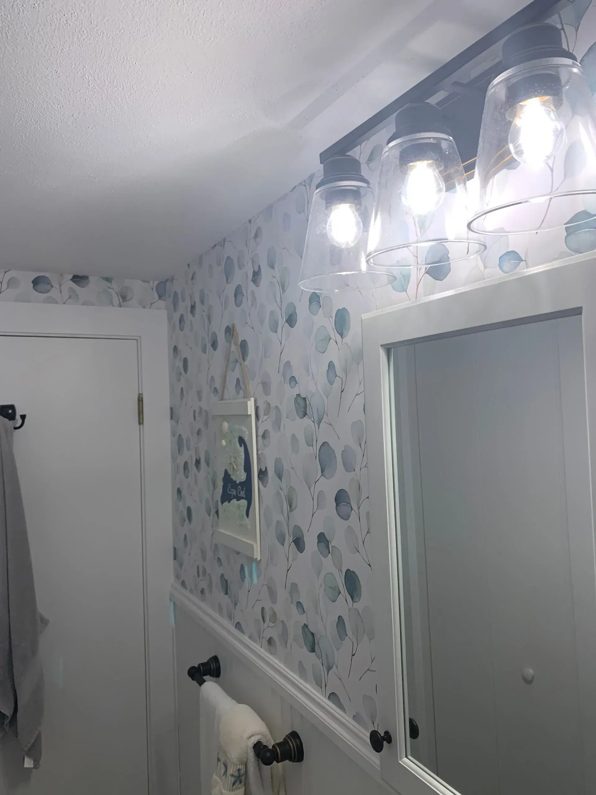 Bathroom with seashell wallpaper, white trim, mirror, and a black light fixture.