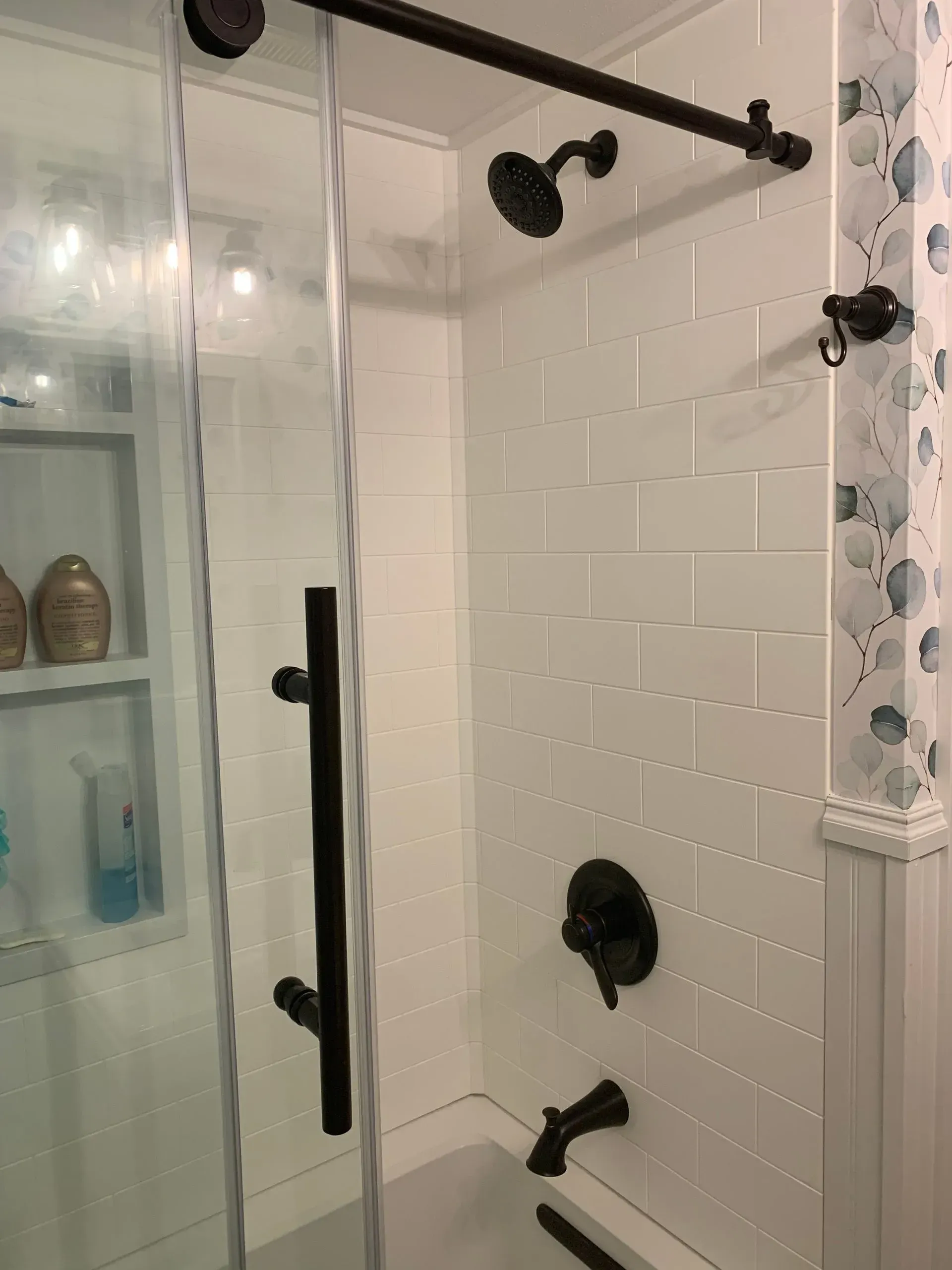 Bathroom shower with white subway tile, dark fixtures, and glass door.