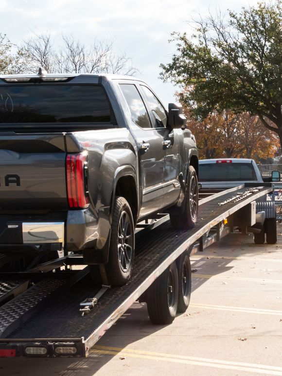Silver pickup truck on a flatbed tow truck, parked outdoors on a sunny day.