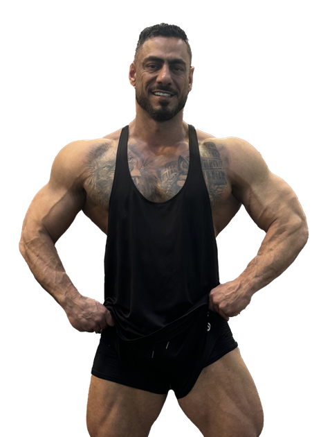 A man is standing with his hands on his hips wearing a black tank top and black shorts.