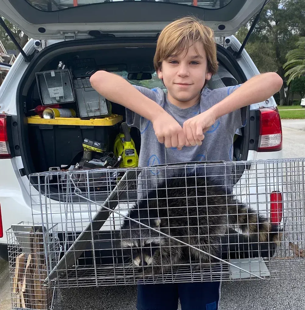 Person leaning on a metal pet crate in an open SUV trunk, smiling outdoors on gravel