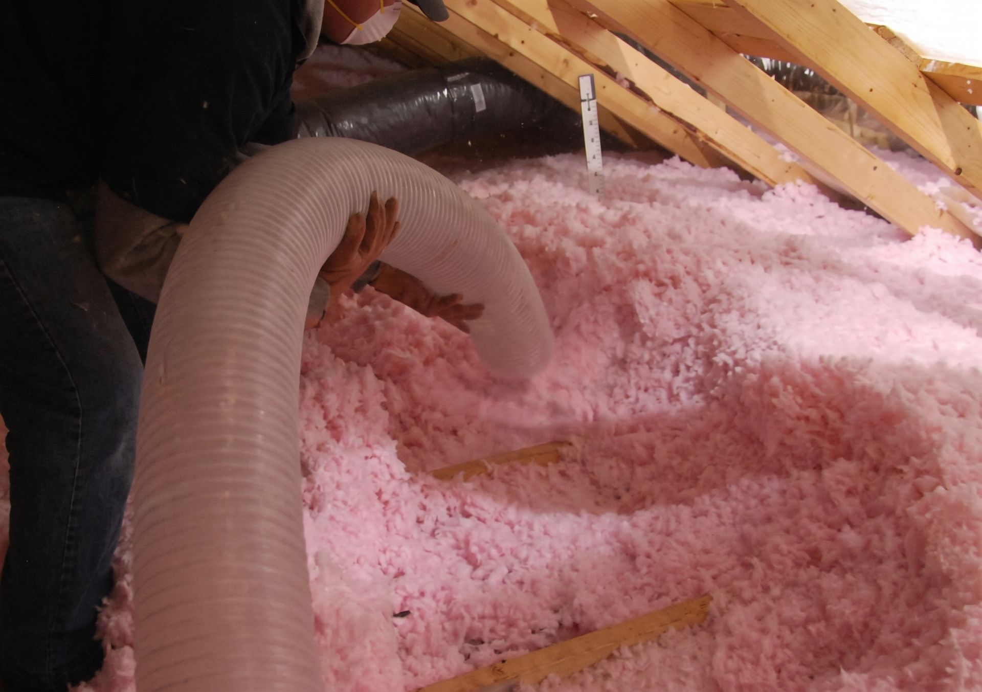 Pink insulation in an attic with a flexible duct and wooden rafters