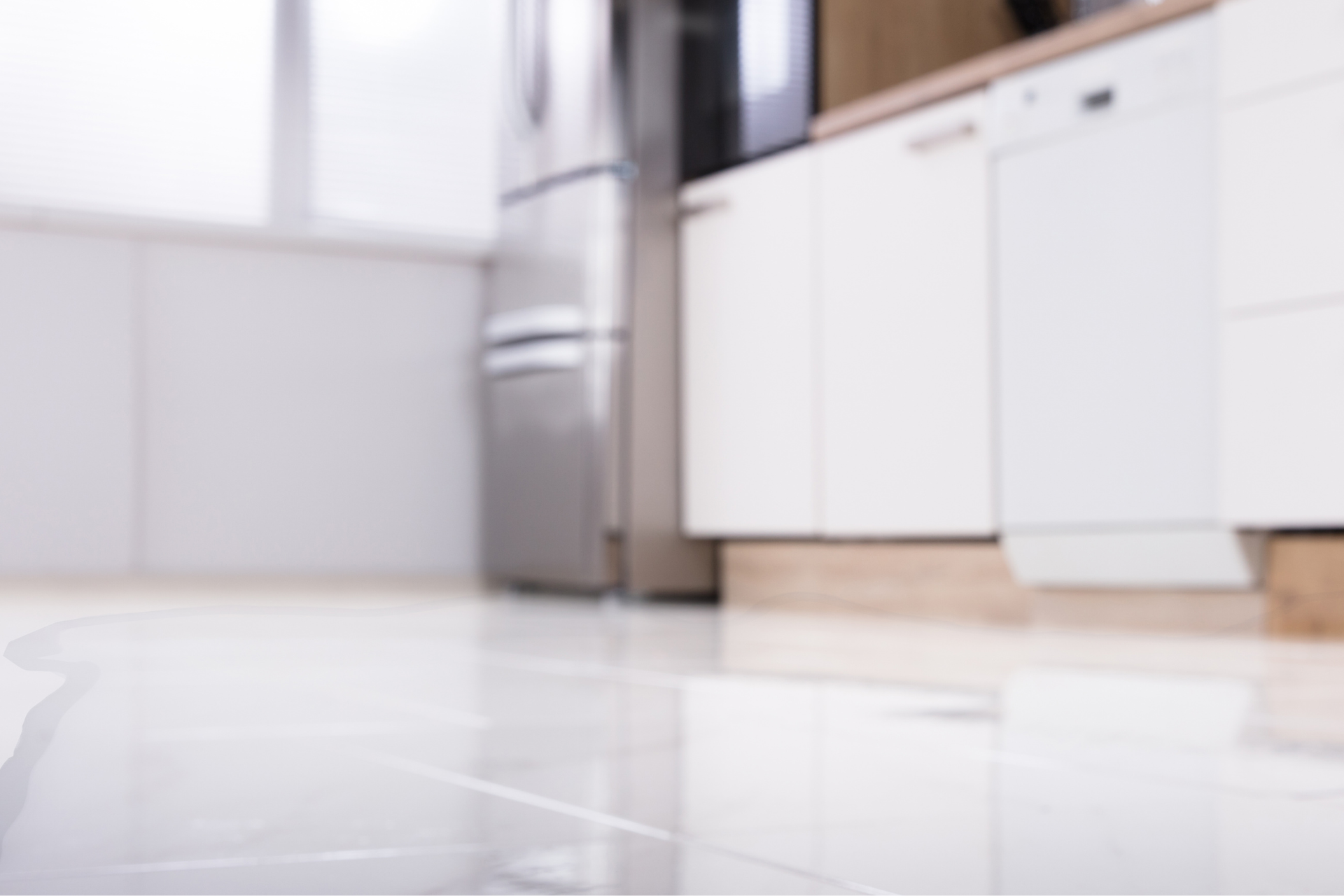 Bright white kitchen floor with cabinets and a stainless steel refrigerator in the background