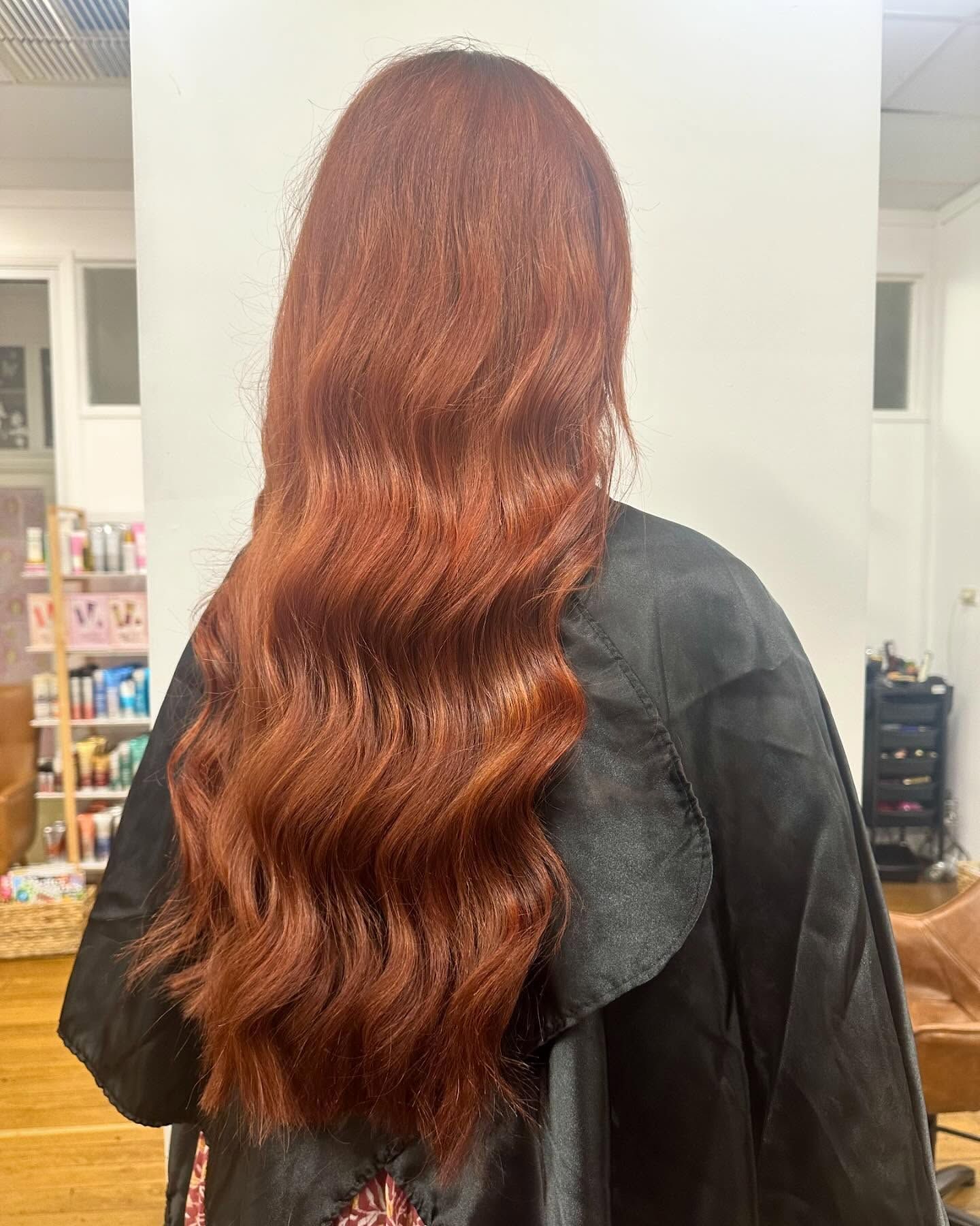 Person with long wavy auburn hair seen from behind in a salon setting — Pose Hair Design in Orange, NSW