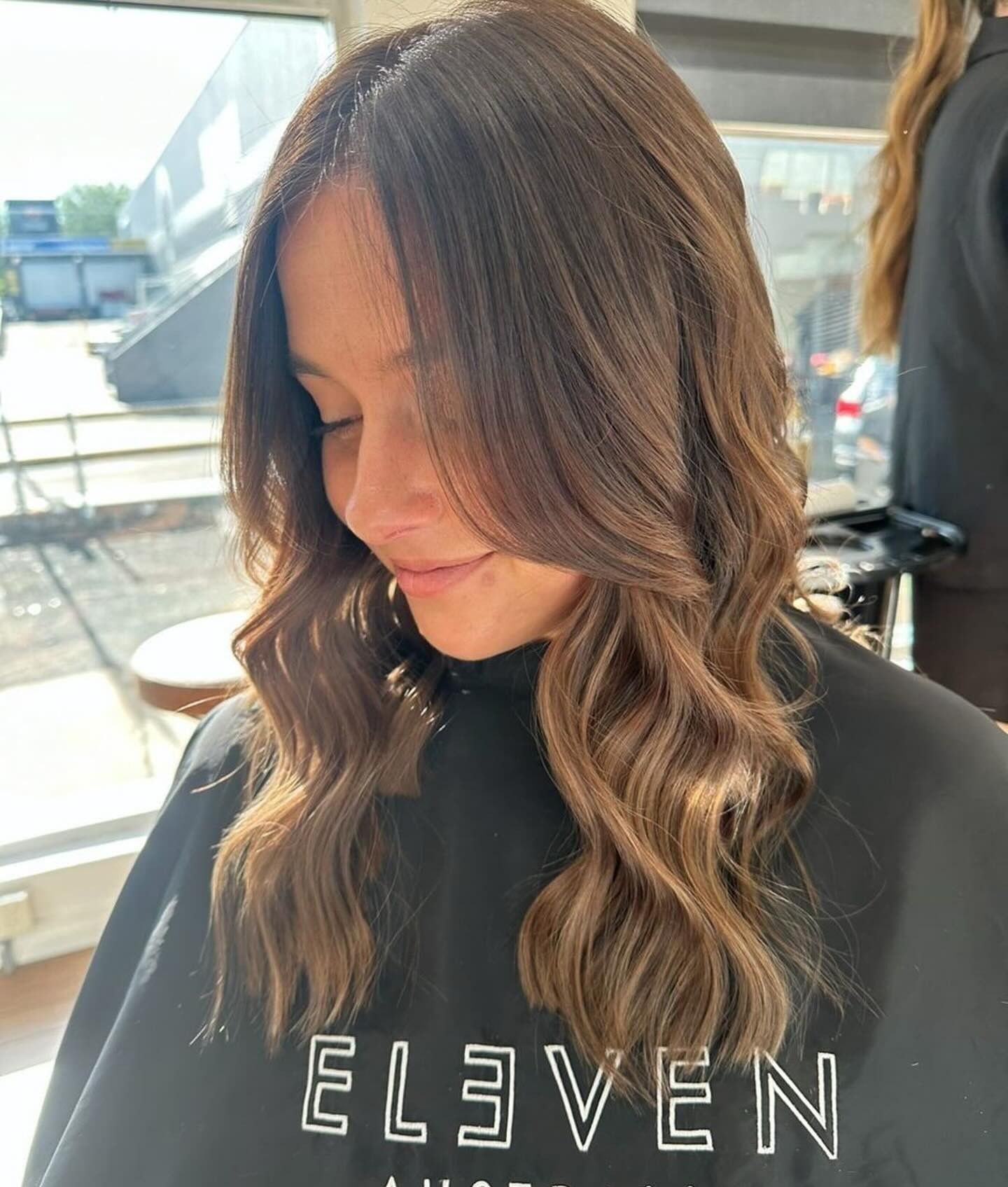 Woman with Wavy Brown Hair in A Black Eleven Sweatshirt — Pose Hair Design in Orange, NSW