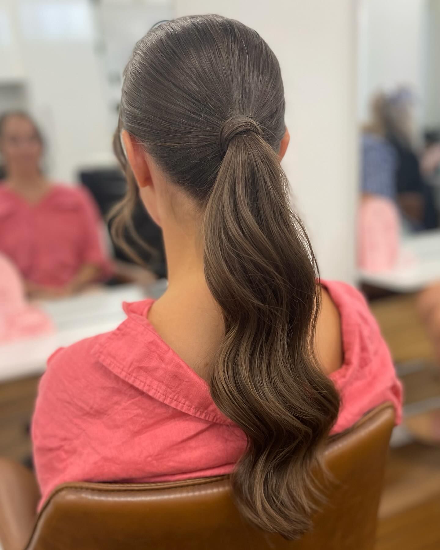Person with dark hair in a low ponytail, wearing a pink top, seated indoors in a classroom or workshop — Pose Hair Design in Orange, NSW
