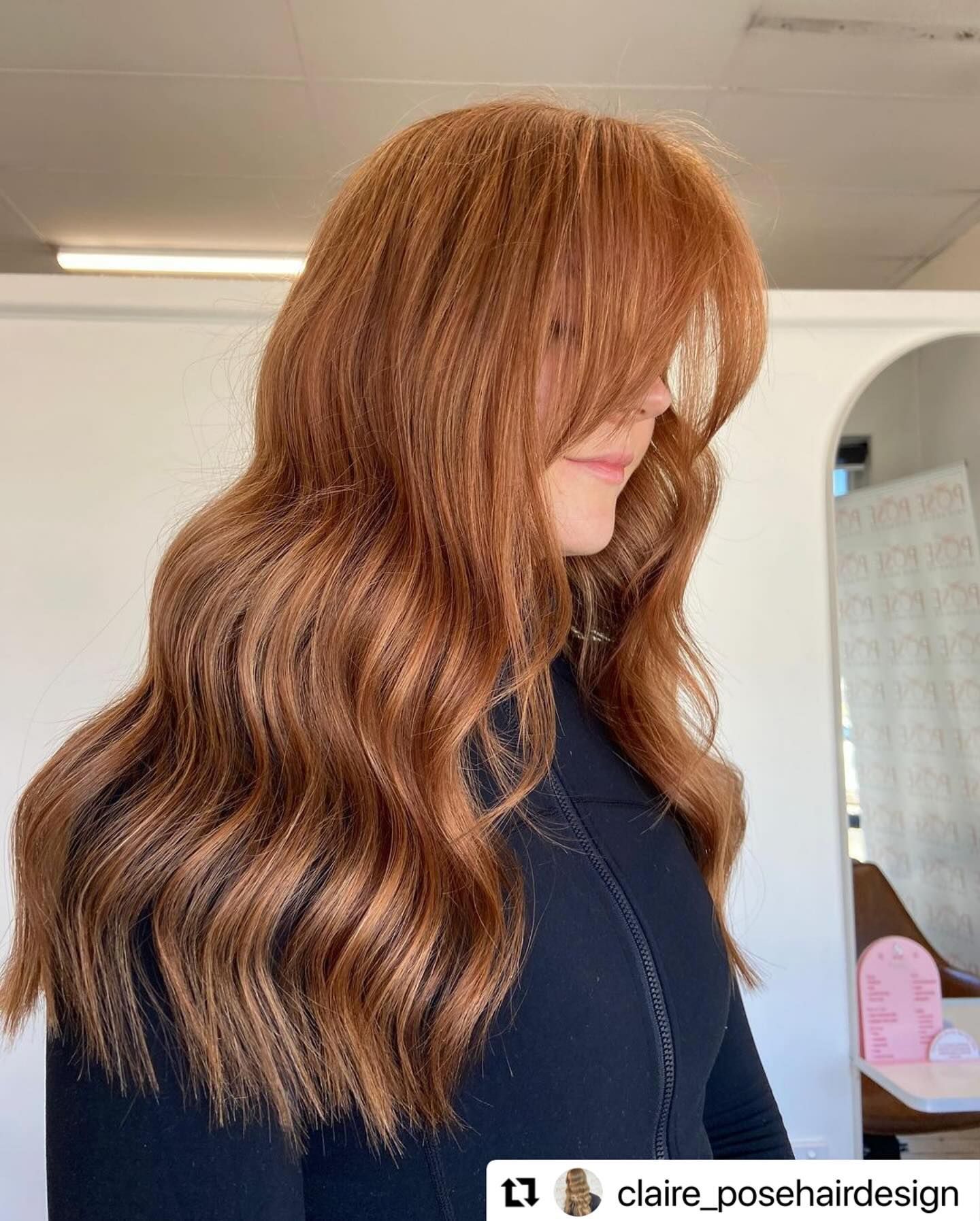 Side-view of long, wavy copper hair with bangs in a bright salon interior — Pose Hair Design in Orange, NSW
