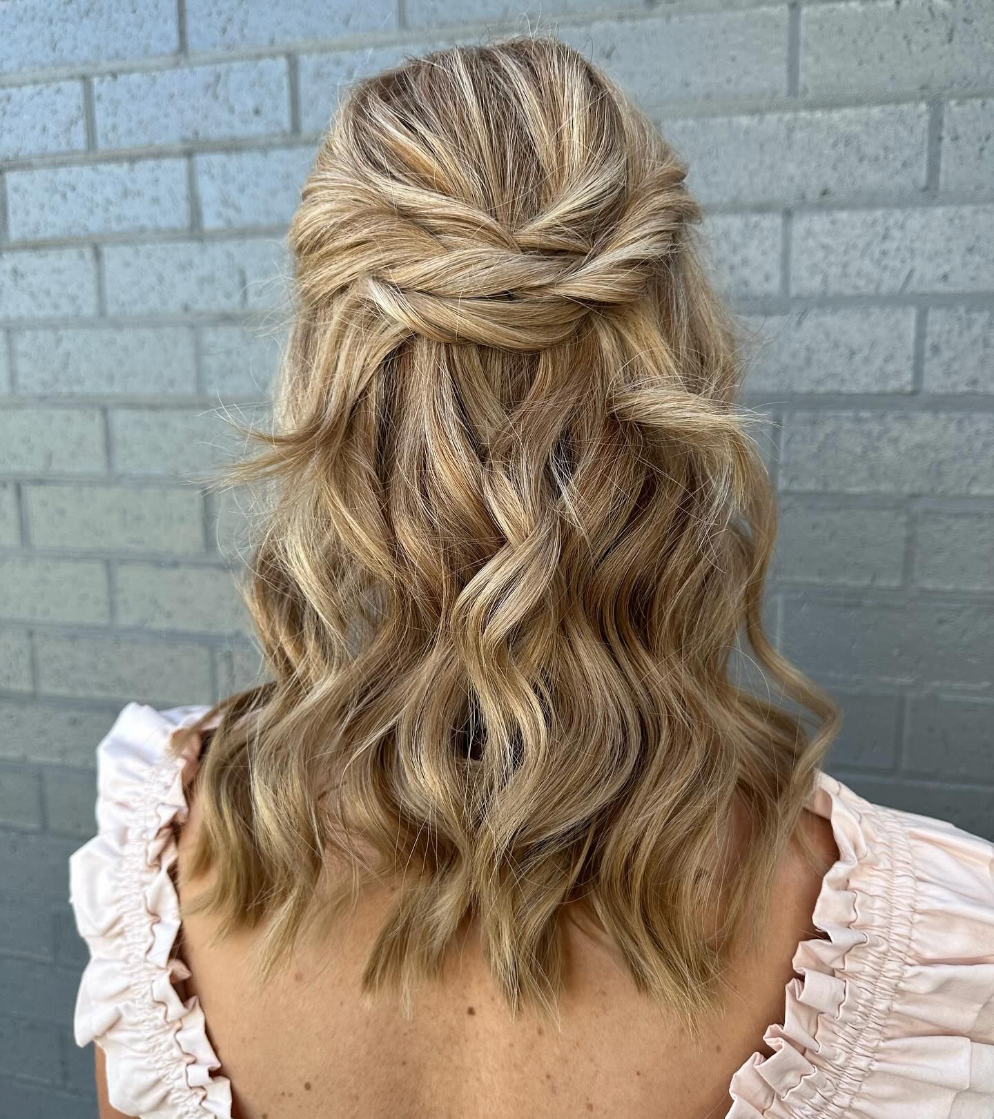 Blonde Wavy Half-Up Hairstyle with Twisted Detail Against a Grey Brick Wall — Pose Hair Design in Orange, NSW