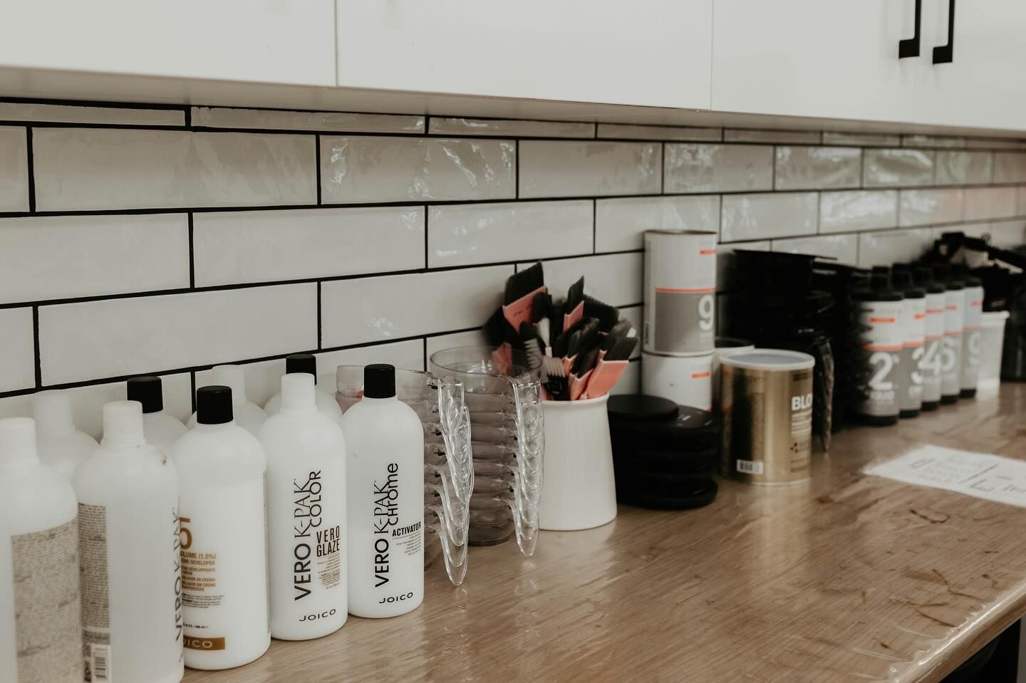 Row of White Product Bottles and Jars on A Wooden Counter in A Tiled Salon or Spa Workspace — Pose Hair Design in Orange, NSW