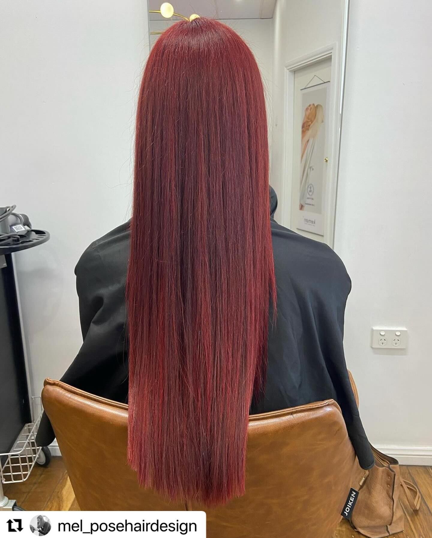 Back view of a person with long straight burgundy hair seated in a salon chair