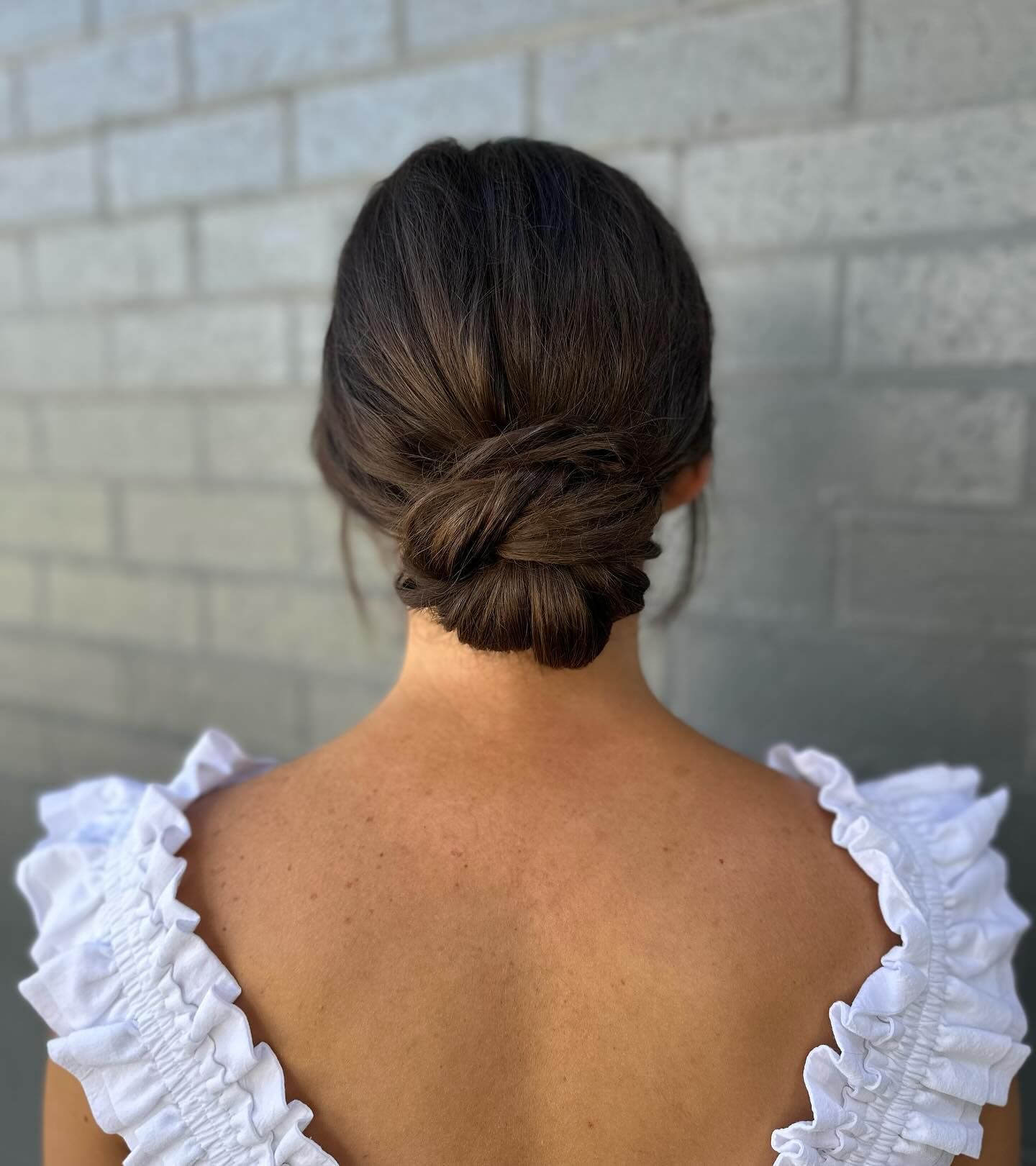 Back view of a low bun hairstyle with loose twists, framed by a white ruffled blouse collar — Pose Hair Design in Orange, NSW