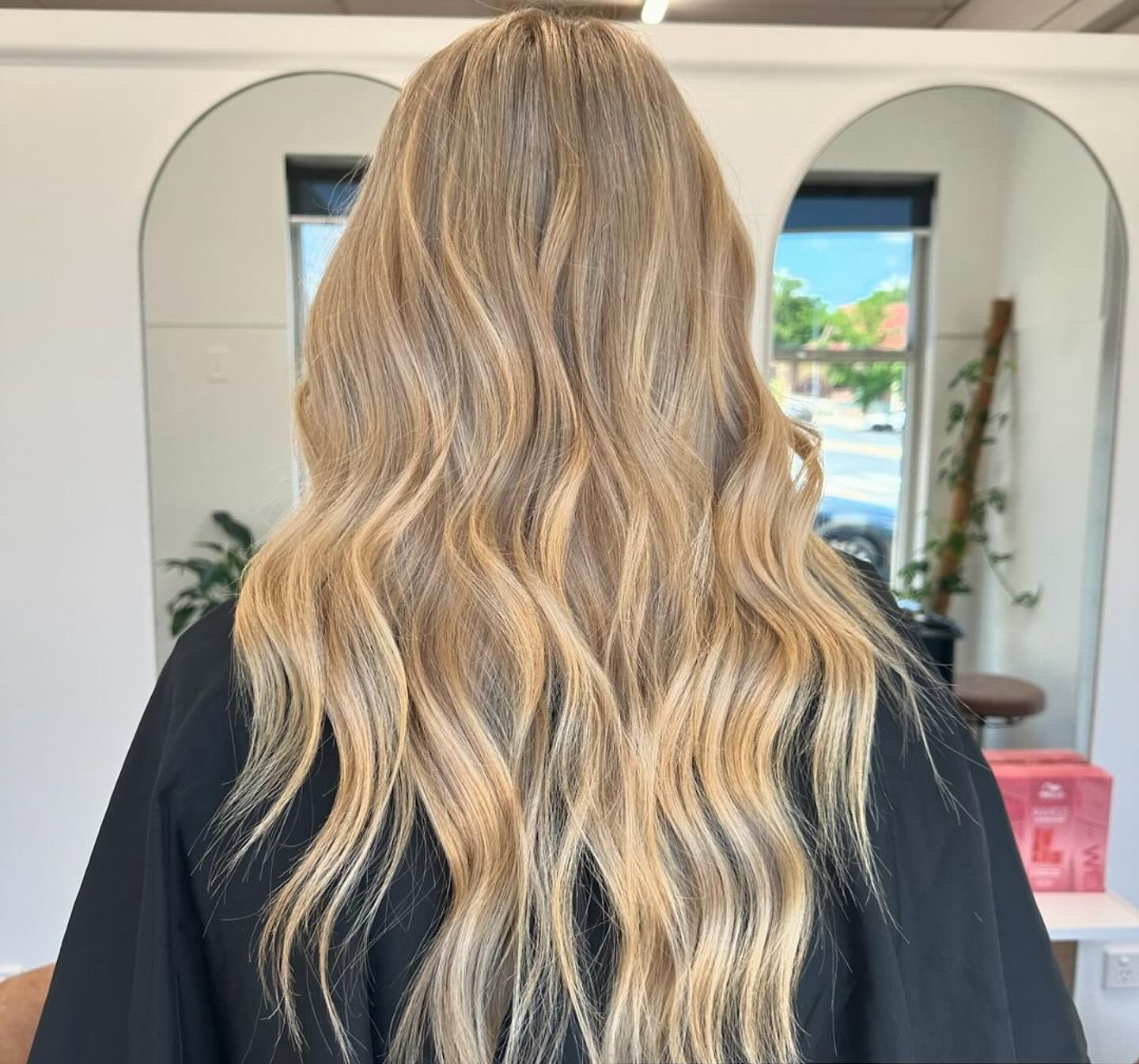 Back view of long, wavy blonde hair with dark roots in a salon setting — Pose Hair Design in Orange, NSW