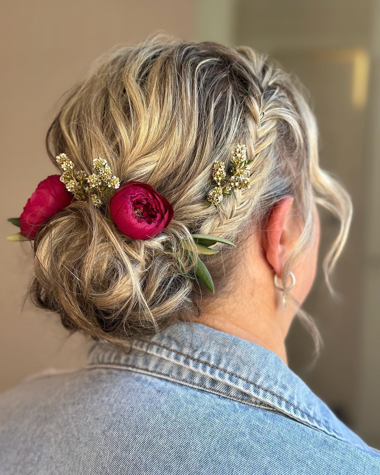 Braided updo with red flowers and green sprigs, seen from the back against a neutral background — Pose Hair Design in Orange, NSW