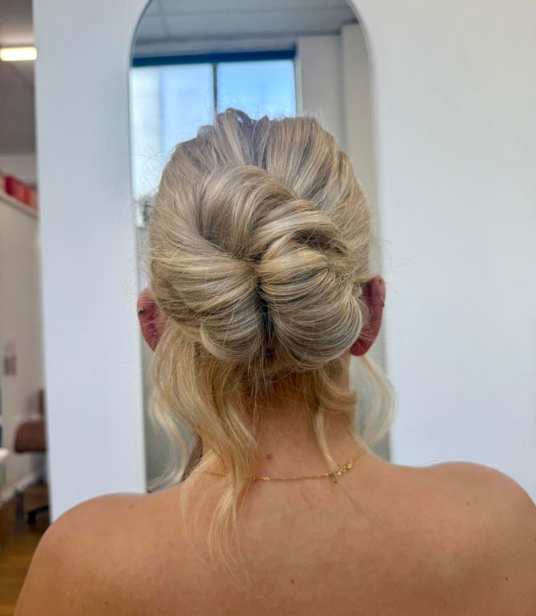 Blonde hair styled in a twisted low bun, viewed from behind in a salon mirror — Pose Hair Design in Orange, NSW