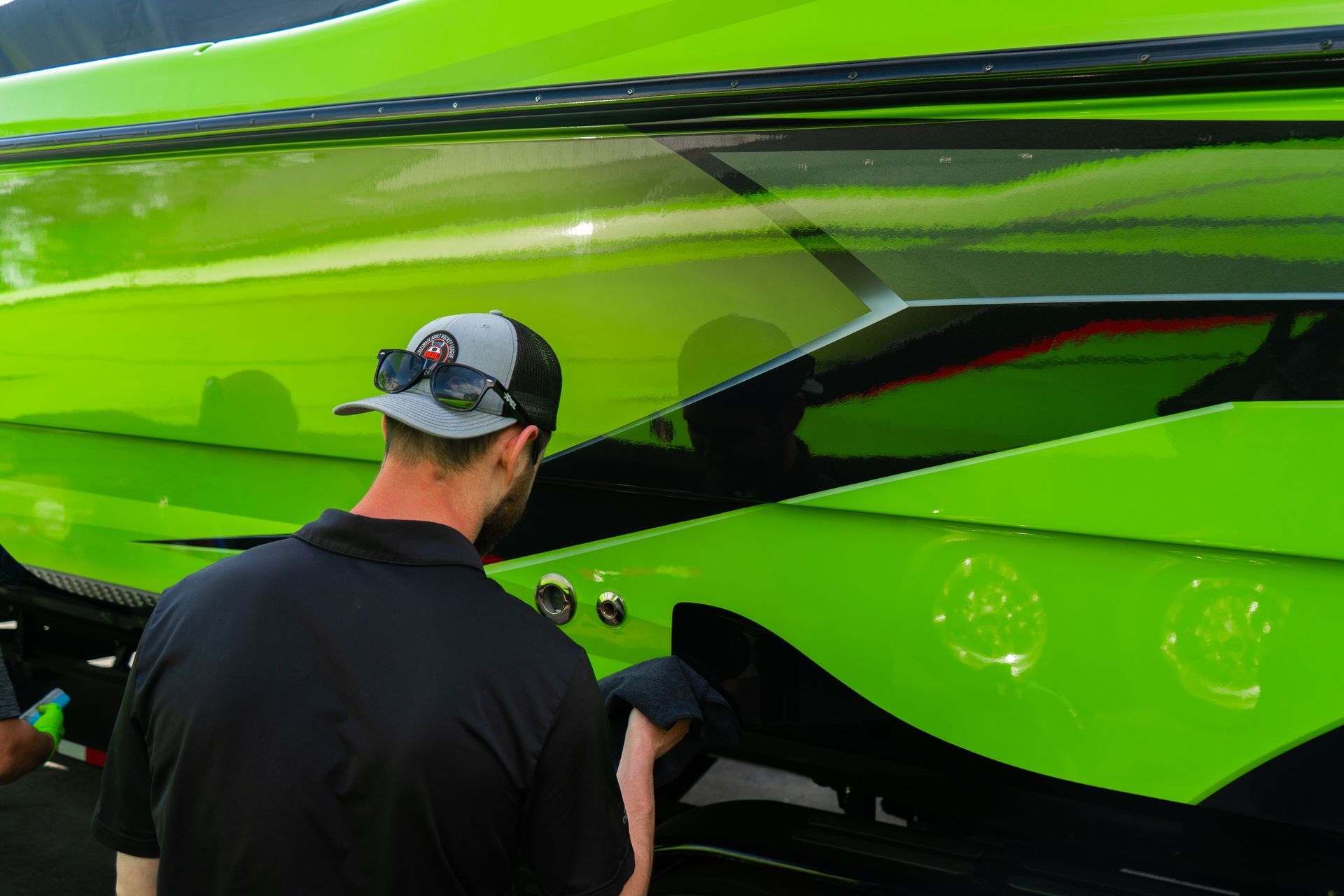Man inspecting a bright green speedboat's hull, outdoor setting.