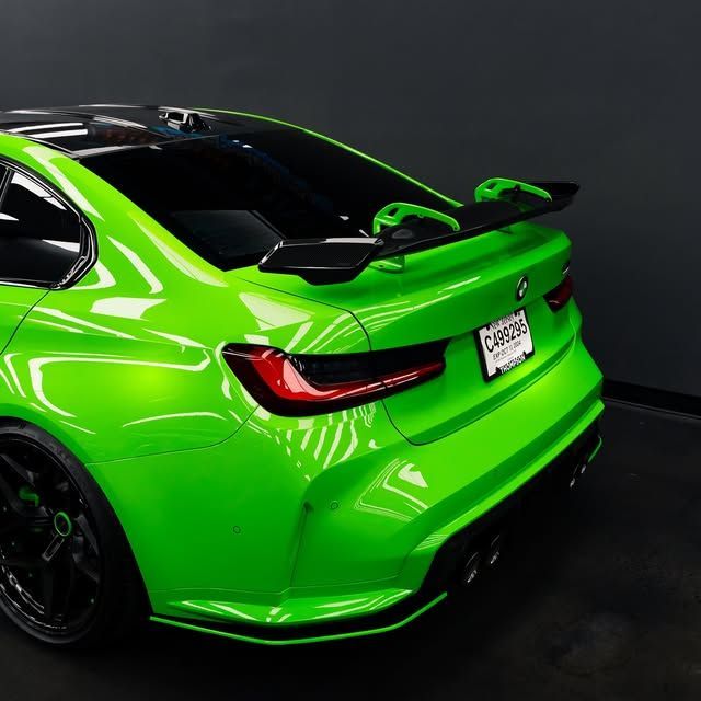 Bright green BMW sports car with black accents and a spoiler, indoors against a dark background.