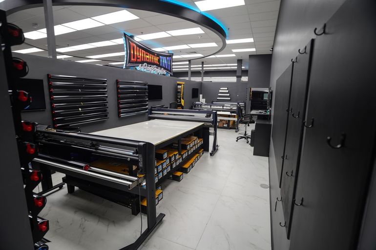 Interior shop with cutting tables and rolls of material, illuminated with overhead lighting.