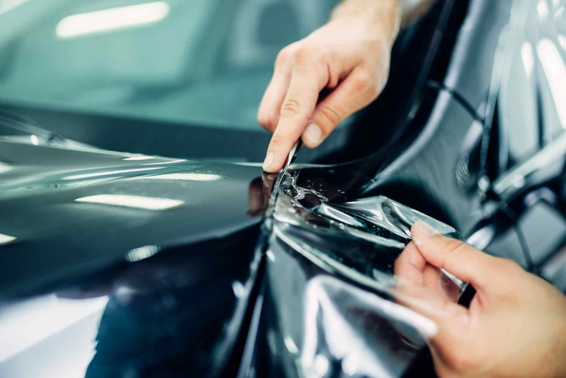 A person is wrapping a car with plastic wrap.