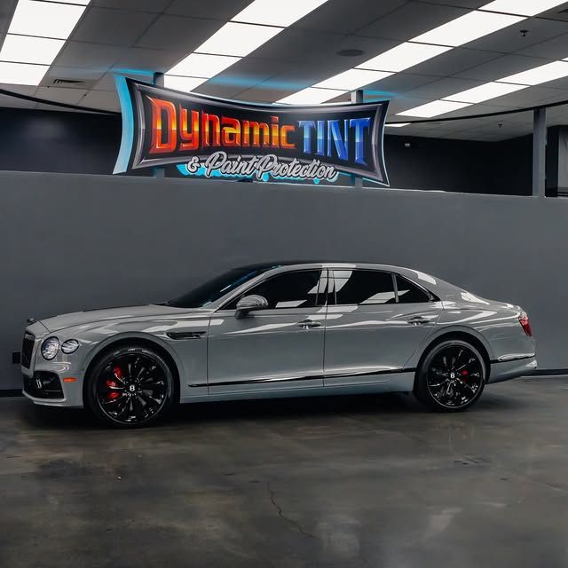 Gray Bentley sedan with tinted windows in a shop with a Dynamic Tint sign.