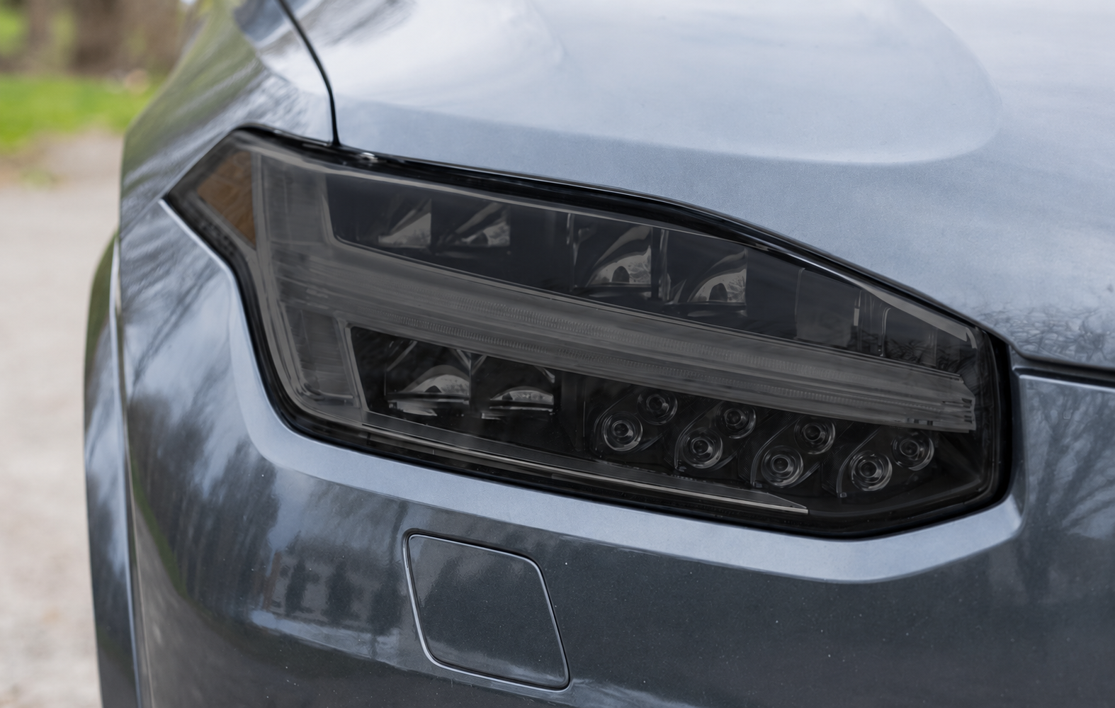 Close-up of a silver Tesla's front end, showing headlight, side mirror, and grill.