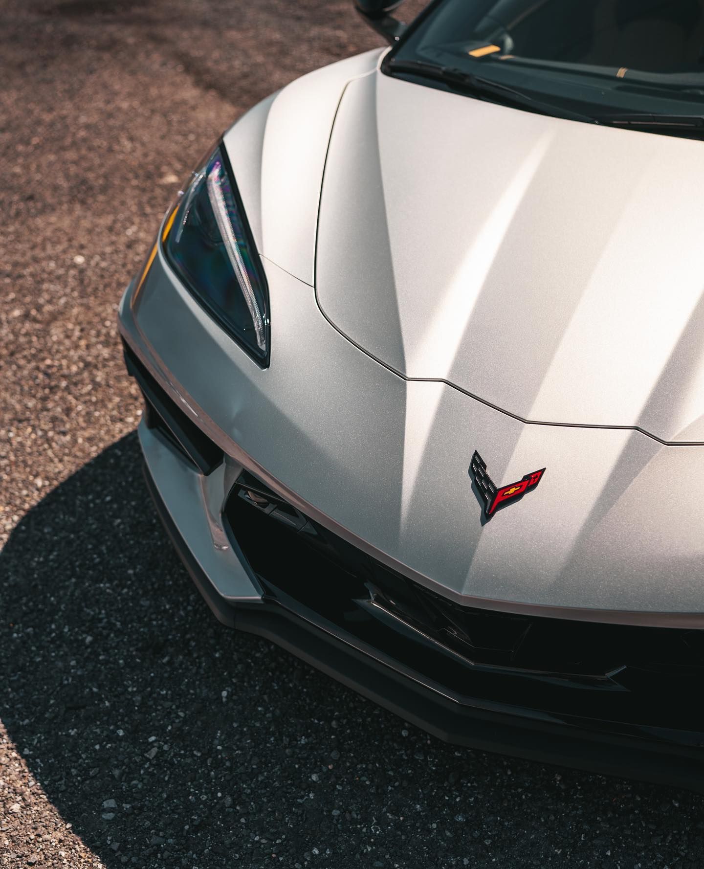White Corvette sports car, front view, on asphalt; a red Chevrolet emblem is visible.