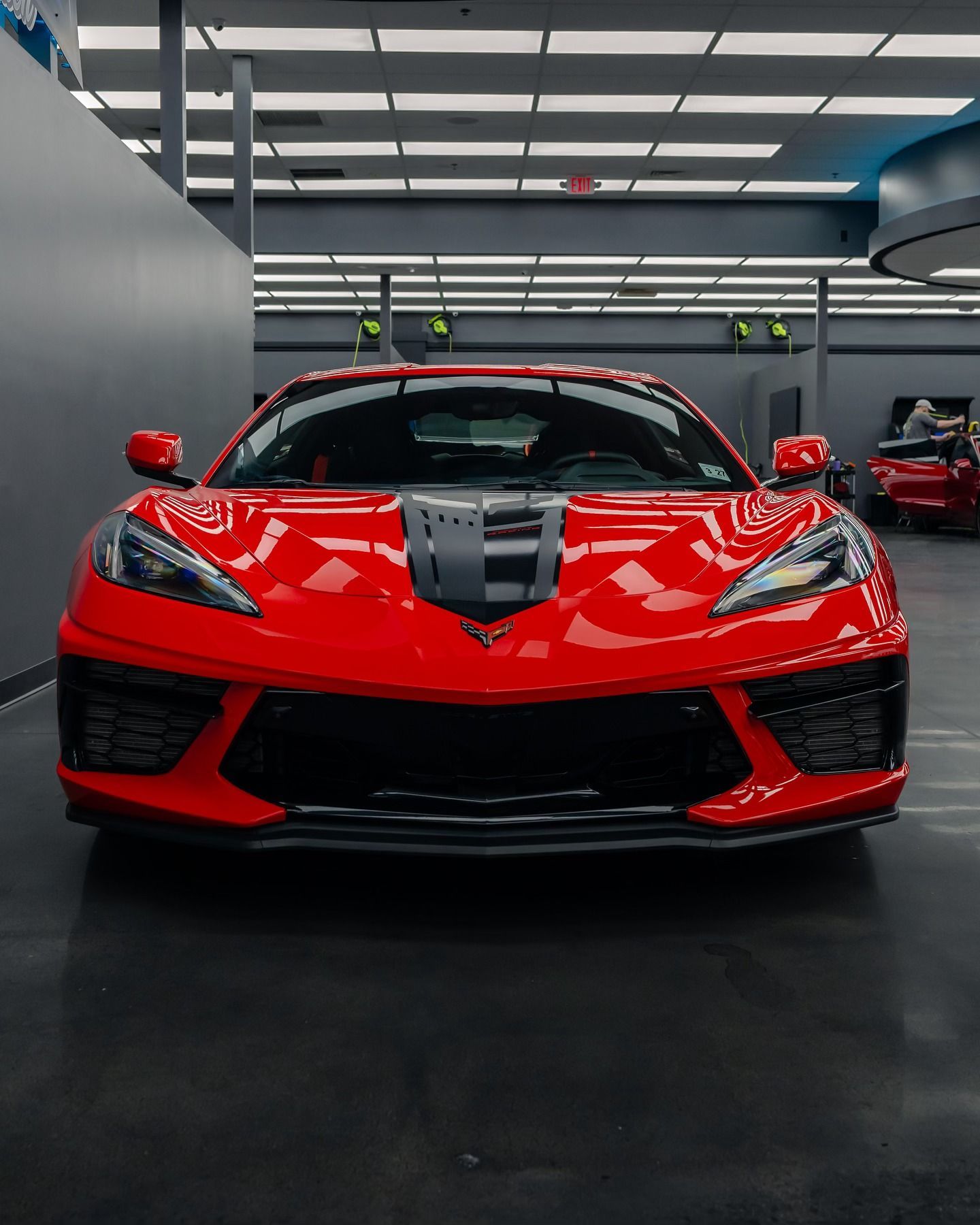 Red Chevrolet Corvette sports car in a showroom with grey racing stripe on hood.