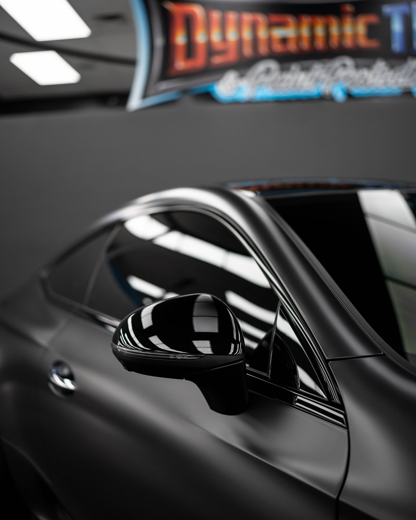 Sleek, gray car with tinted windows and glossy black side mirror, in a car detailing shop.