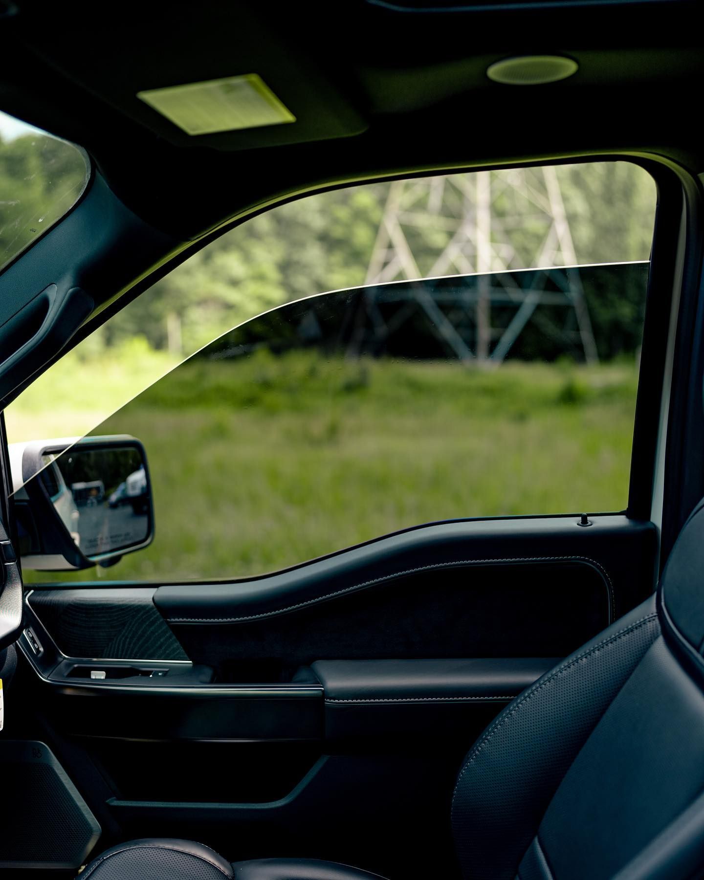 Interior view of a black truck with tinted window overlooking a grassy field and power lines.