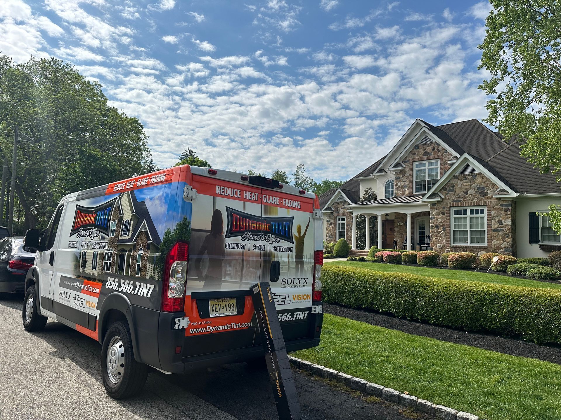 White van with company logo parked in front of a house on a sunny day.