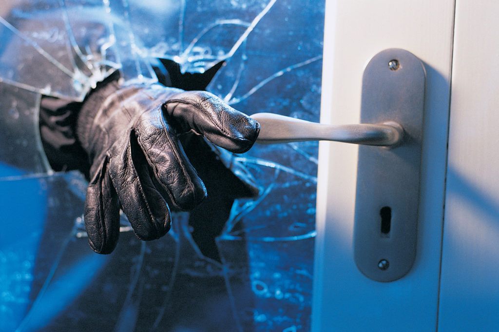 Gloved hand reaching through broken glass to open a door.