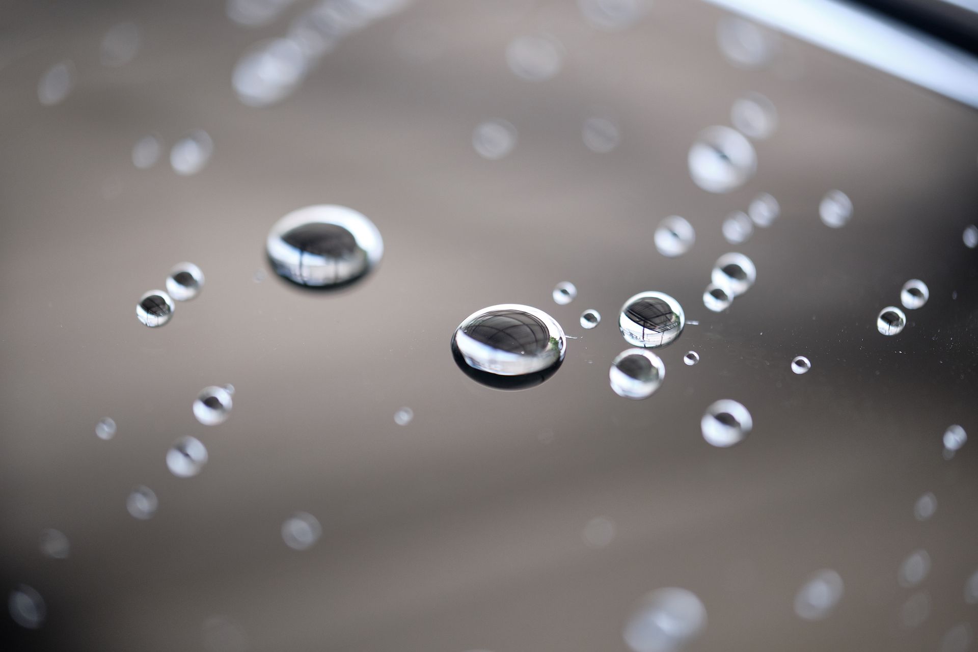 Water droplets on a shiny, dark surface; some droplets reflect light.