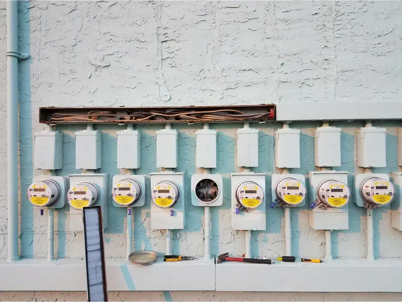Row of gas meters and pipes mounted on a pale wall with a damaged opening above them